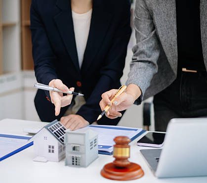 istockphoto-2251295973-612x612 Professional real estate agent discussing property contract with client, showing house model, agreement, and legal consultation for home buying and investment.
